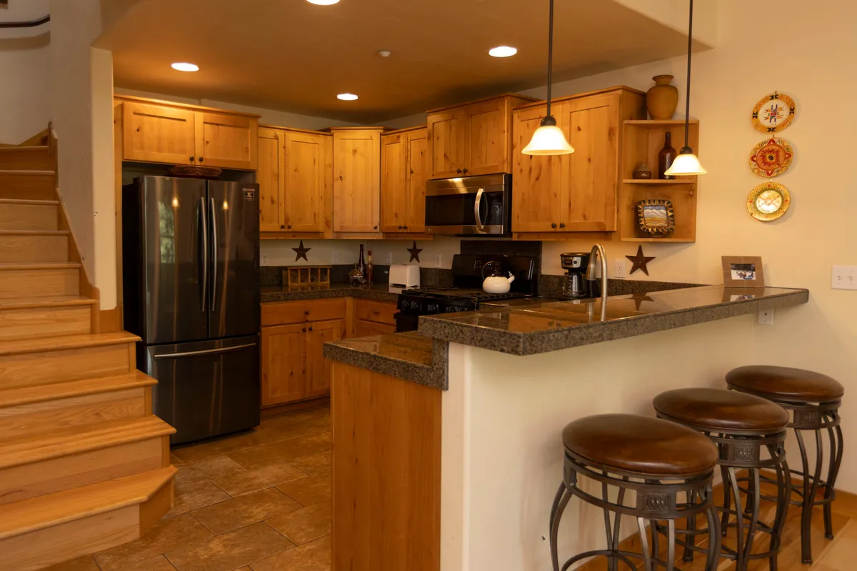 This image showcases a welcoming kitchen with a central island complete with bar stools, stainless steel appliances, and warm wooden cabinetry. The room glows with natural light and a sense of lively activity, suggesting both culinary preparation and social gathering.