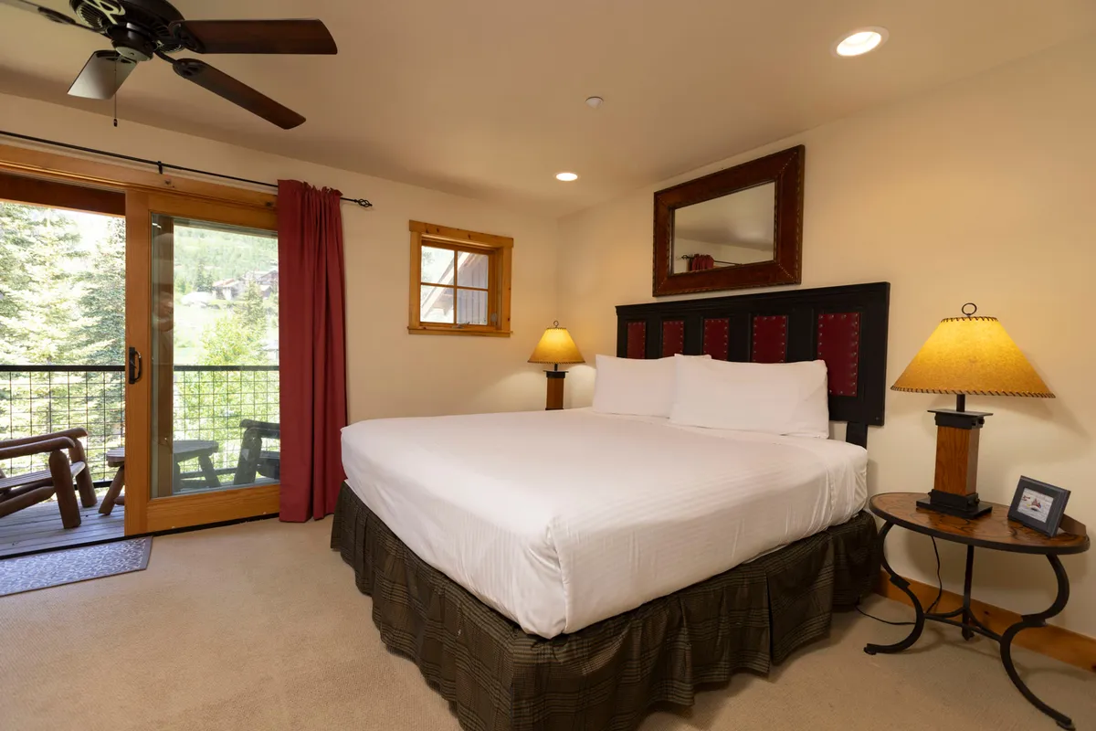 A tranquil bedroom with a comfortable bed, bedside lamps, and doors that open out to a private balcony. The soft lighting and calming colors evoke a sense of peace and relaxation, ideal for unwinding after adventurous days.