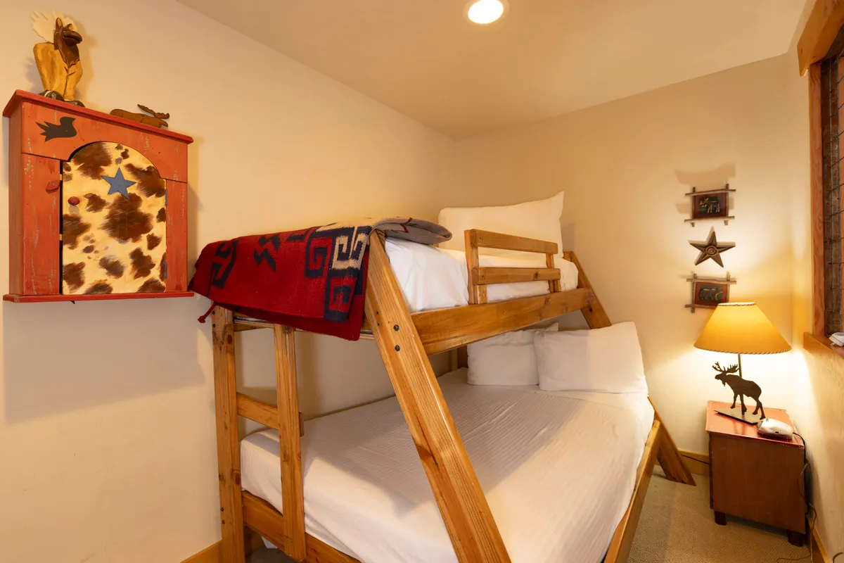 A cozy, inviting bedroom featuring a bunk bed with soft bedding, a decorative shelf, and a reading lamp. The setup is playful yet restful, perfect for children or friends to share stories before drifting off to sleep.