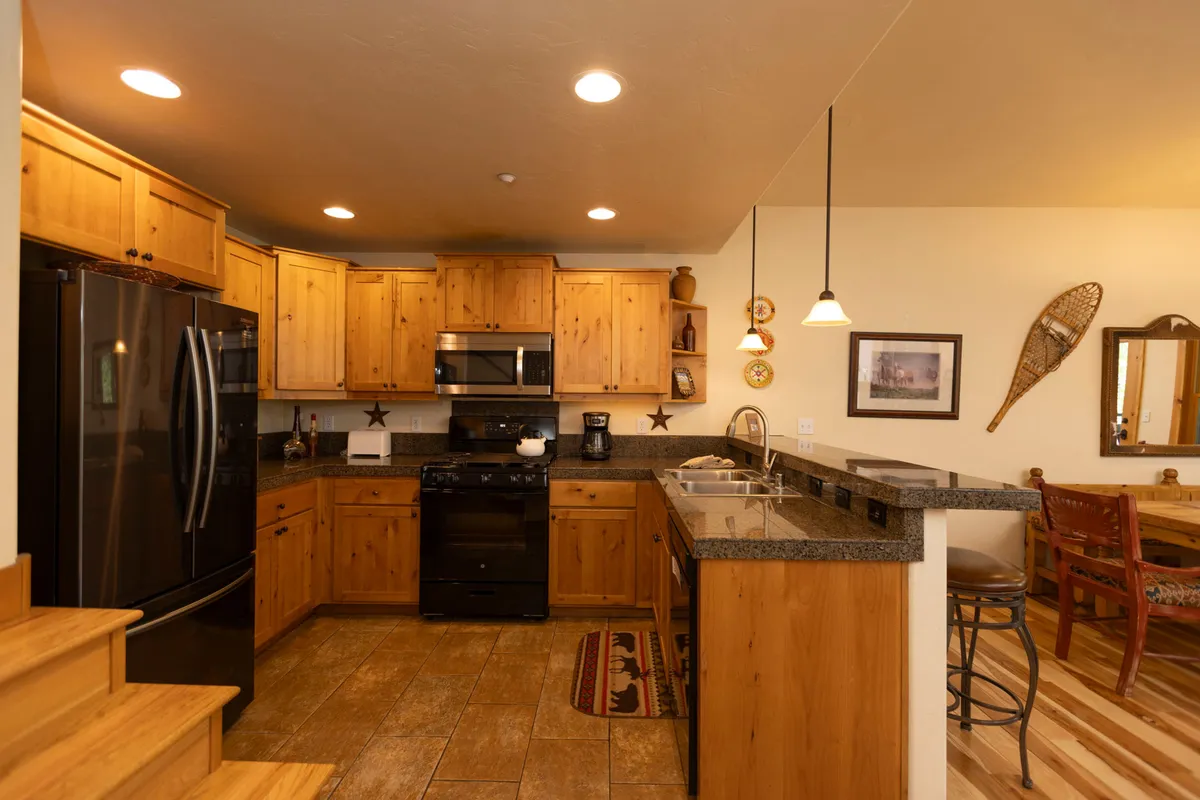 A view of the kitchen featuring stainless steel appliances, dark granite countertops, and wooden cabinetry, with decorative wall items adding a personal touch. The space exudes warmth, ideal for preparing meals after outdoor adventures.