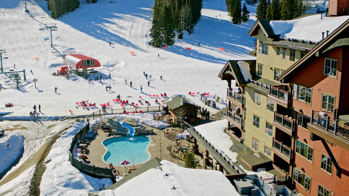 A lively scene showing ski slopes and a swimming pool at a mountain resort, with a lodge and ski lift visible. The area is bustling with activity and framed by sunset light, encapsulating both adventure and relaxation.