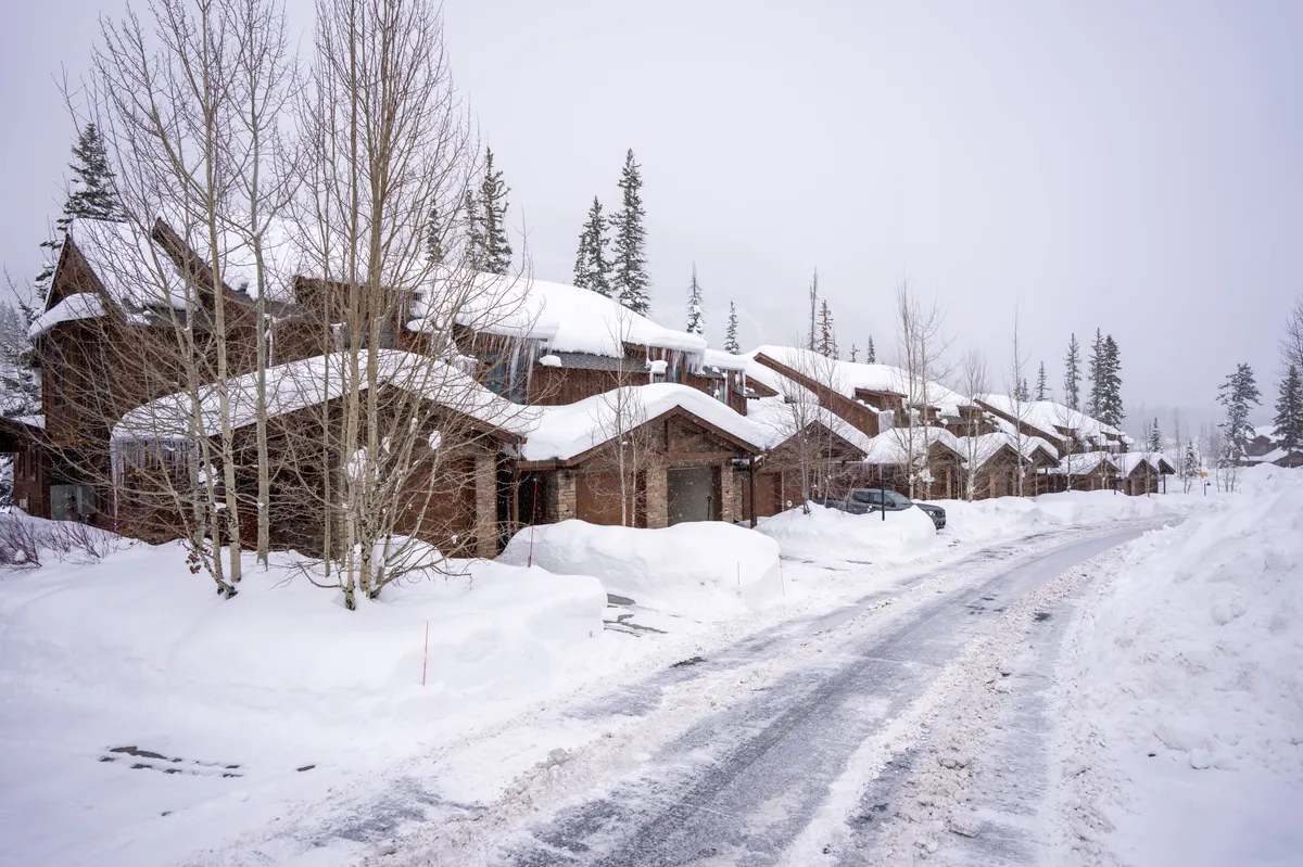A row of snow-covered cottages lines a peaceful road, framed by bare trees under a winter sky. The scene evokes tranquility, with hints of outdoor fun like snowman-building and gathering by the fire after a snowy day.
